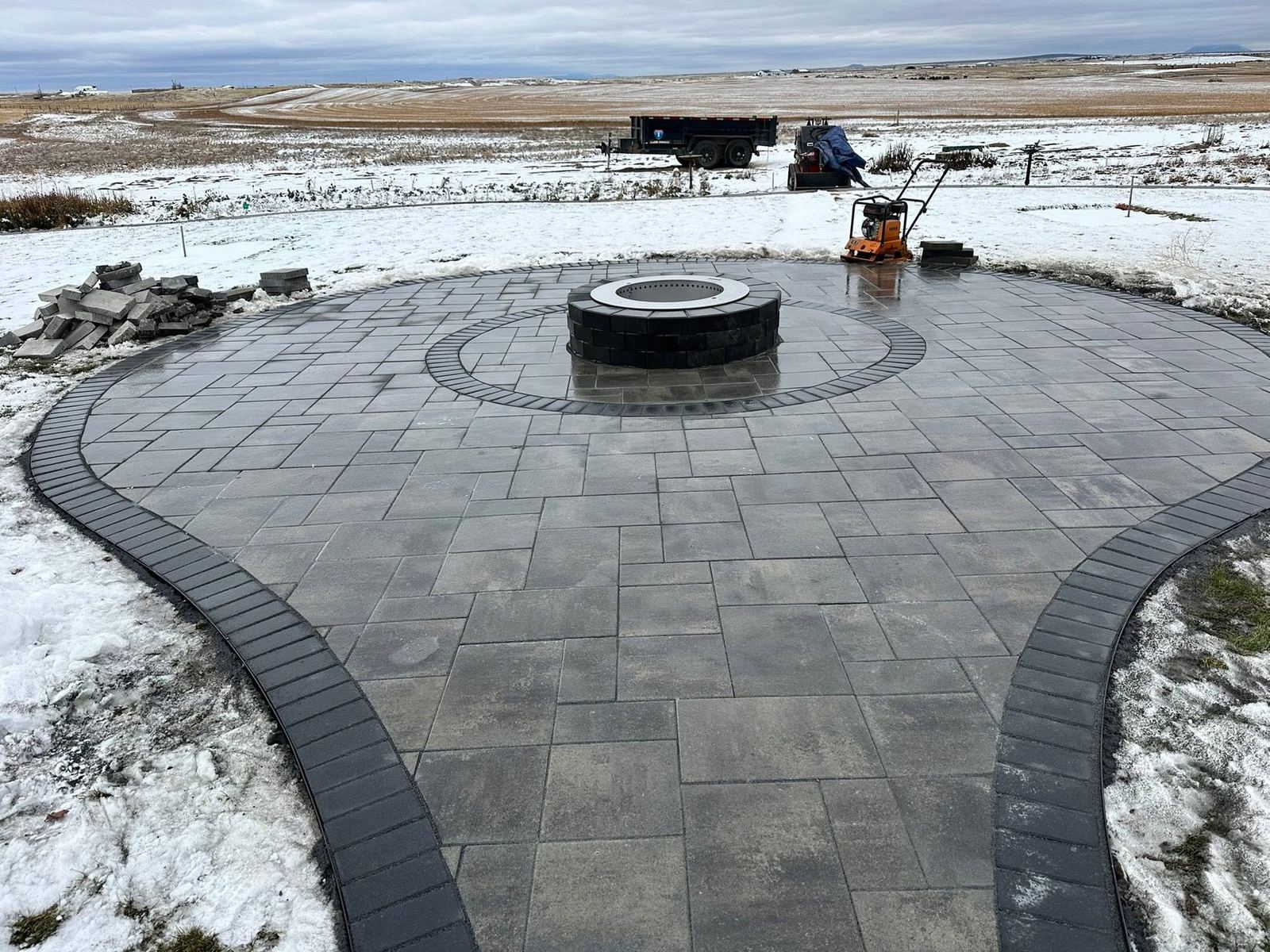 Circular grey paver patio with a built-in firepit and soldier-course border